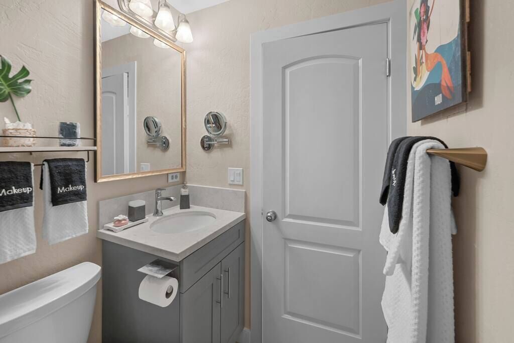 A bathroom with a toilet, sink, mirror, towel rack, and a door.