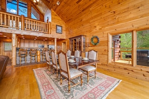 A wooden cabin interior with a dining area, kitchen, and a balcony.