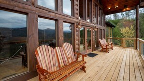 Ett trädäck med Adirondack-stolar och stora fönster med utsikt över ett bergigt landskap.