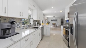 Eine moderne Küche mit weißen Schränken, einem Edelstahlkühlschrank, einem eingebauten Backofen und einer Kaffeemaschine.