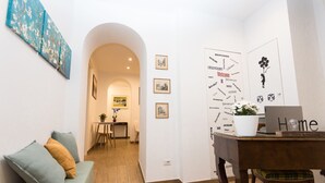 Une pièce chaleureuse avec un canapé vert, une table en bois sur laquelle se trouve un ordinateur portable, et un mur orné de tableaux et d’une pancarte de bienvenue.