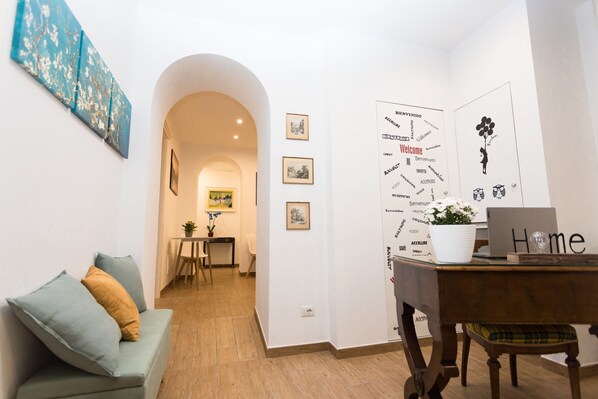 A cozy room with a green sofa, a wooden table with a laptop, and a wall with framed pictures and a welcome sign. - Dreaming in Rome (Rome)