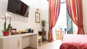Une chambre d’hôtel avec un lit, un bureau avec une télévision, une plante en pot et une fenêtre avec des rideaux.