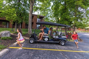 A golf cart with passengers, a pedestrian, and a building in the background. - Willow – Lakefront Luxe w/ Resort Access on Table Rock Lake (Branson)
