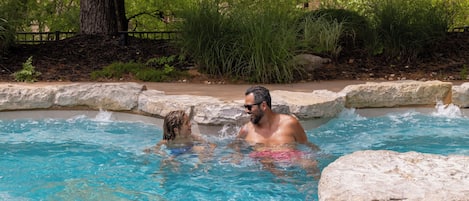 Una piscina de agua azul cristalina, rodeada de vegetación natural y muros de piedra.