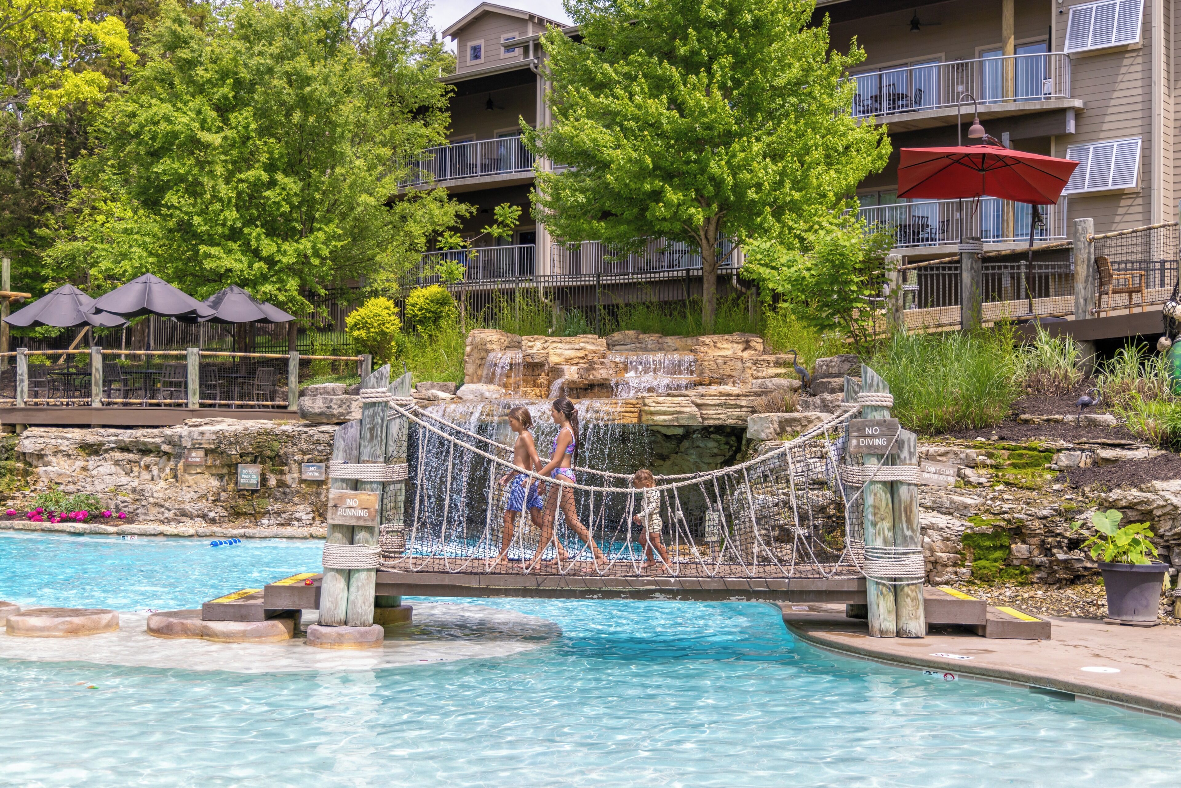 A pool area with a rock bridge, a wooden fence, and a sign indicating no diving.