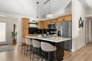 Una cocina moderna con una isla central, taburetes de bar, un refrigerador de acero inoxidable y un microondas.