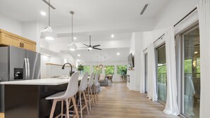 Una cocina moderna con una isla central, taburetes de bar y una zona de comedor con vistas al exterior.