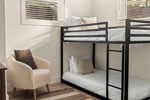 Una cama litera con dos niveles, una silla con cojín y una ventana con persianas.