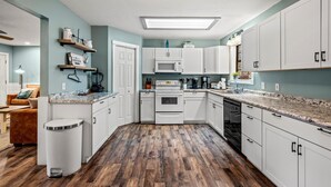 A kitchen with white cabinets, a microwave, an oven, and a dishwasher. There is a countertop with a sink and a trash can.