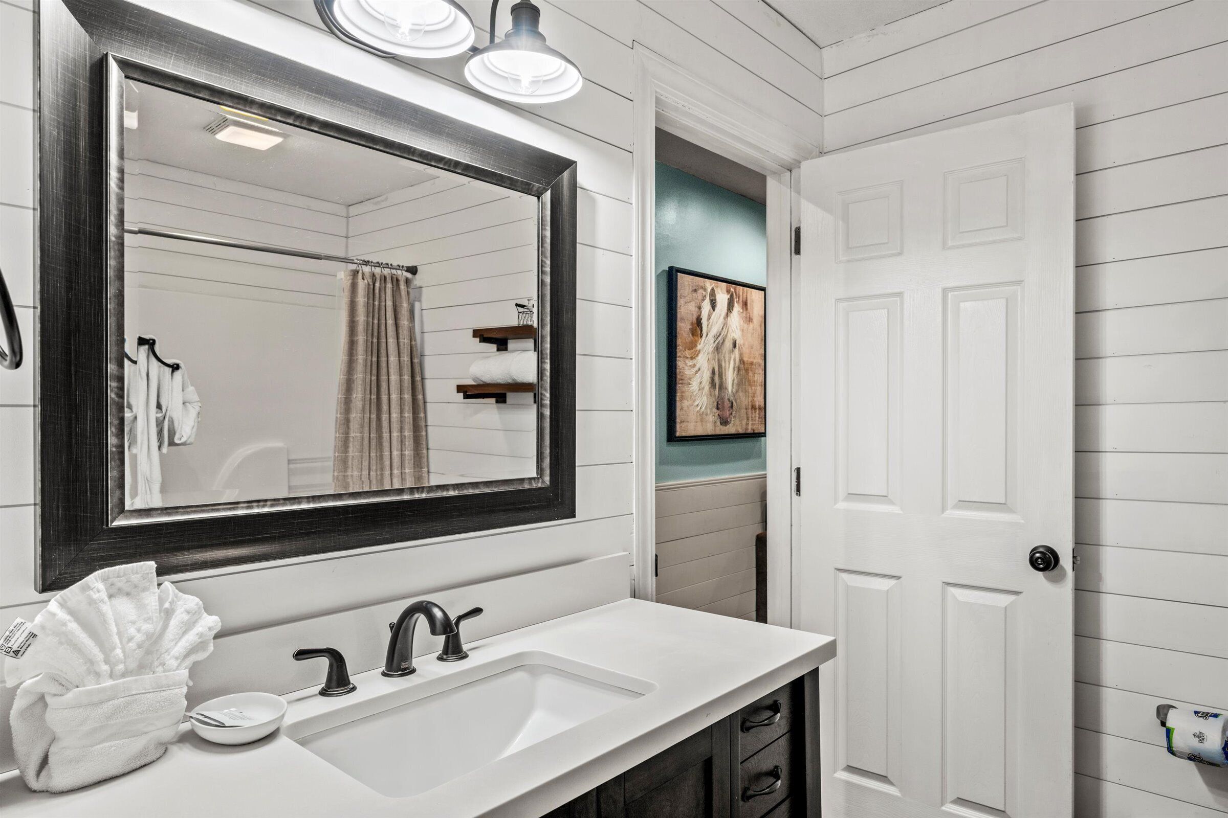 Un baño con un lavabo blanco, un espejo grande y una puerta que da a la zona de la ducha.