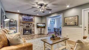 A cozy living room with a fireplace, a ceiling fan, and a stone accent wall.