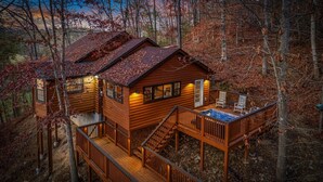 A wooden cabin with a hot tub on a deck, surrounded by trees.