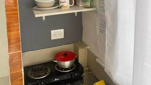 Une petite cuisine équipée d’une cuisinière à gaz, d’étagères où sont rangés les ustensiles de cuisine, d’une tasse à café et d’un panier à fruits accroché au mur.