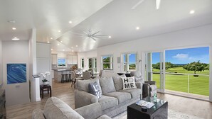 Ein geräumiges Wohnzimmer mit grauem Sofa, einem Couchtisch und Blick auf einen Golfplatz durch große Fenster.