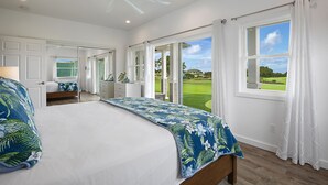 Ein Schlafzimmer mit einem großen Bett, einem Deckenventilator, Blick auf einen Golfplatz durch das Fenster und einer Tür zu einem Badezimmer.