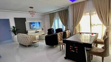 A modern living room with a pool table, comfortable seating, a flat-screen TV, and a large window with curtains.
