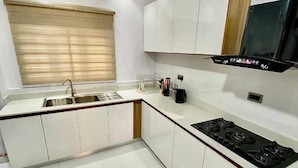 A modern kitchen with white cabinetry, a stainless steel sink, a black stove, and a window with blinds. - Harrington court (Lekki)