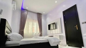 A modern bedroom with a bed, a TV, and a black door. - Harrington court (Lekki)