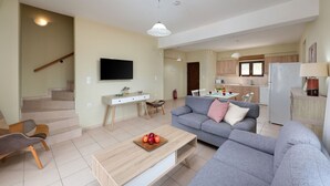 Un soggiorno moderno con un divano grigio, un tavolino in legno con della frutta, una TV a parete e una scala che conduce a un altro livello.