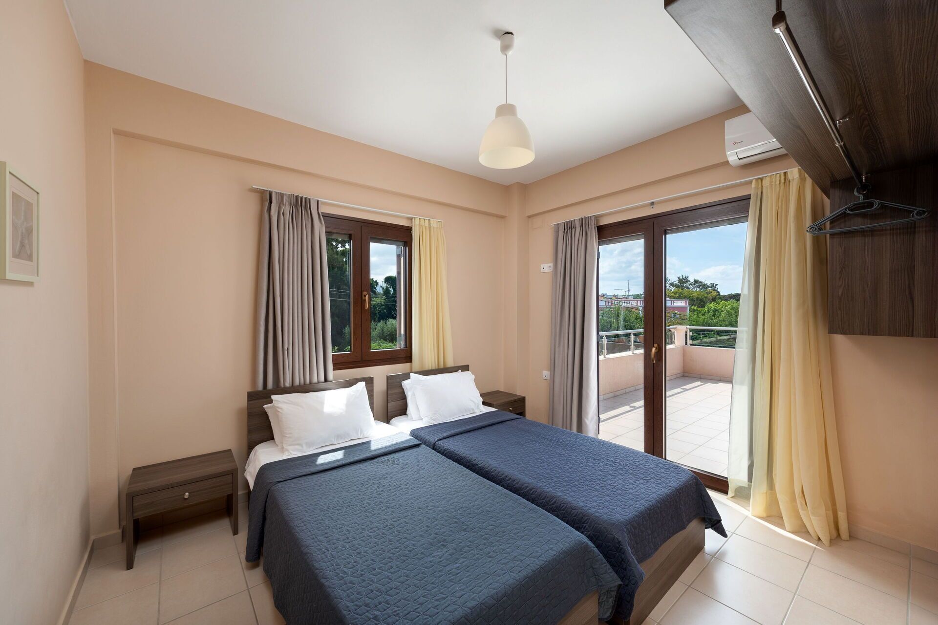 A hotel room with two beds, a ceiling fan, a large window with curtains, and a balcony with a view.