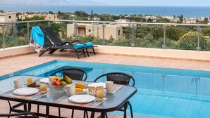 Area pranzo a bordo piscina con tavolo apparecchiato per la colazione, poltrone relax e vista sul mare e sulle montagne.