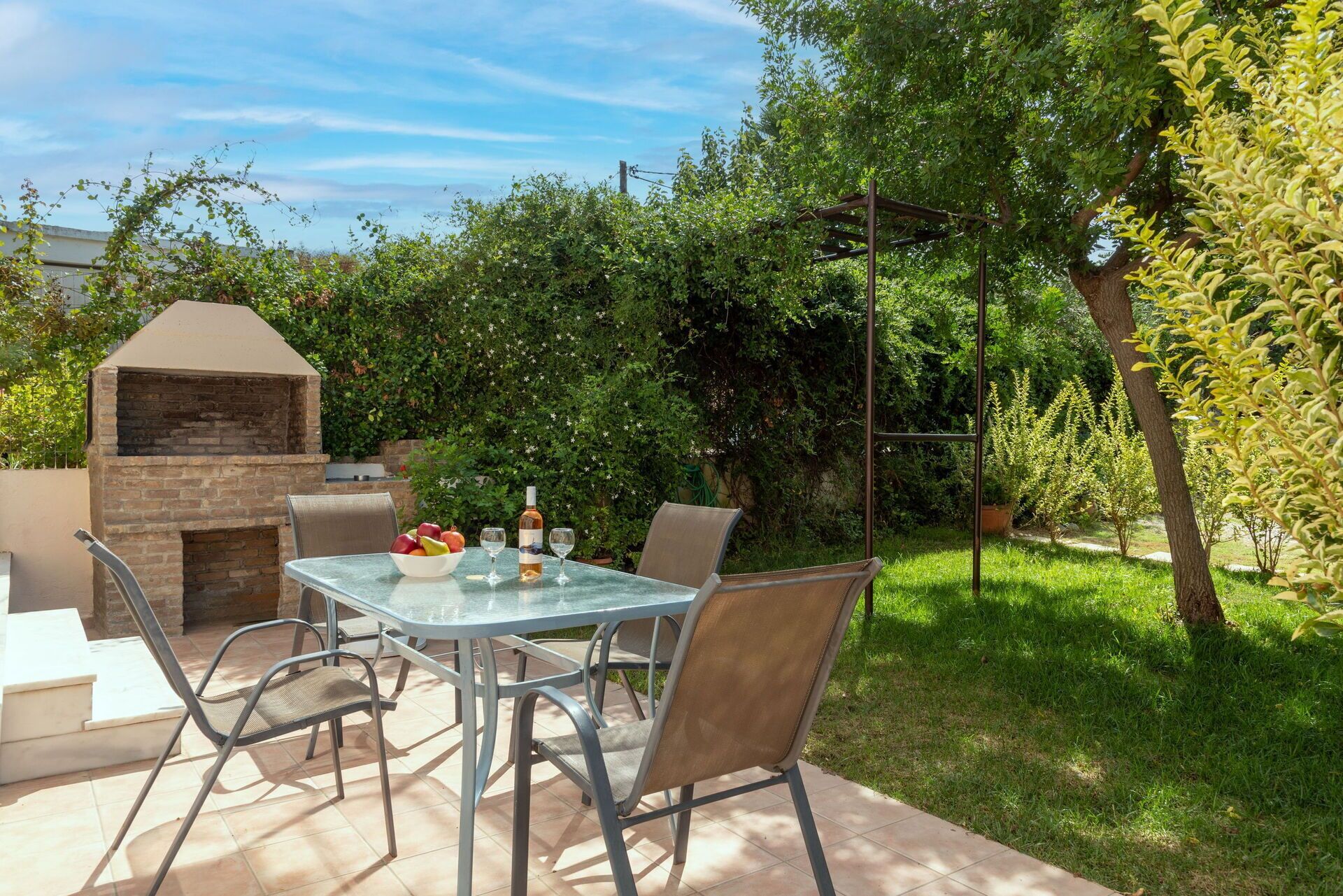 An outdoor patio with a brick barbecue, a glass table, and chairs.