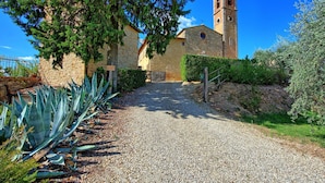 A gravel path leading to a stone building with a bell tower, surrounded by greenery and a clear blue sky. - Camino, Montauto - Holiday apartment  with pool close to San Gimignano (Montauto)