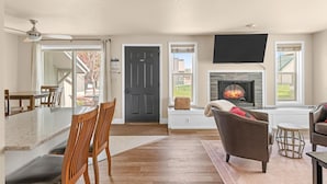 A spacious living room with a fireplace, a dining area with a large table and chairs, and a TV mounted on the wall.