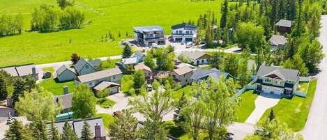 An aerial view of a residential area with houses, a swimming pool, and a forested landscape.