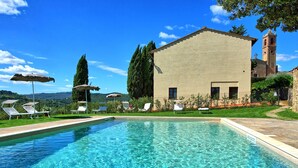 A swimming pool with lounge chairs and umbrellas, a building with a tower, and a view of hills. - Villa, Montauto - Vacation Villa with pool close to San Gimignano (Montauto)