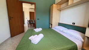 Une chambre d’hôtel avec un lit, une couvre-lit verte, des oreillers blancs et une armoire en bois.