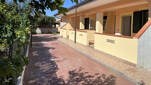 Un espace extérieur abrité avec un chemin pavé, un bâtiment jaune doté d’un toit en tuiles et un mur avec une fenêtre.