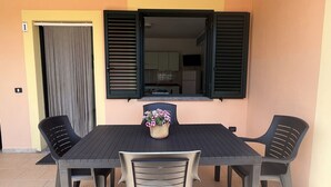 Un coin repas comprenant une table et quatre chaises, une plante en pot et une fenêtre avec des volets.