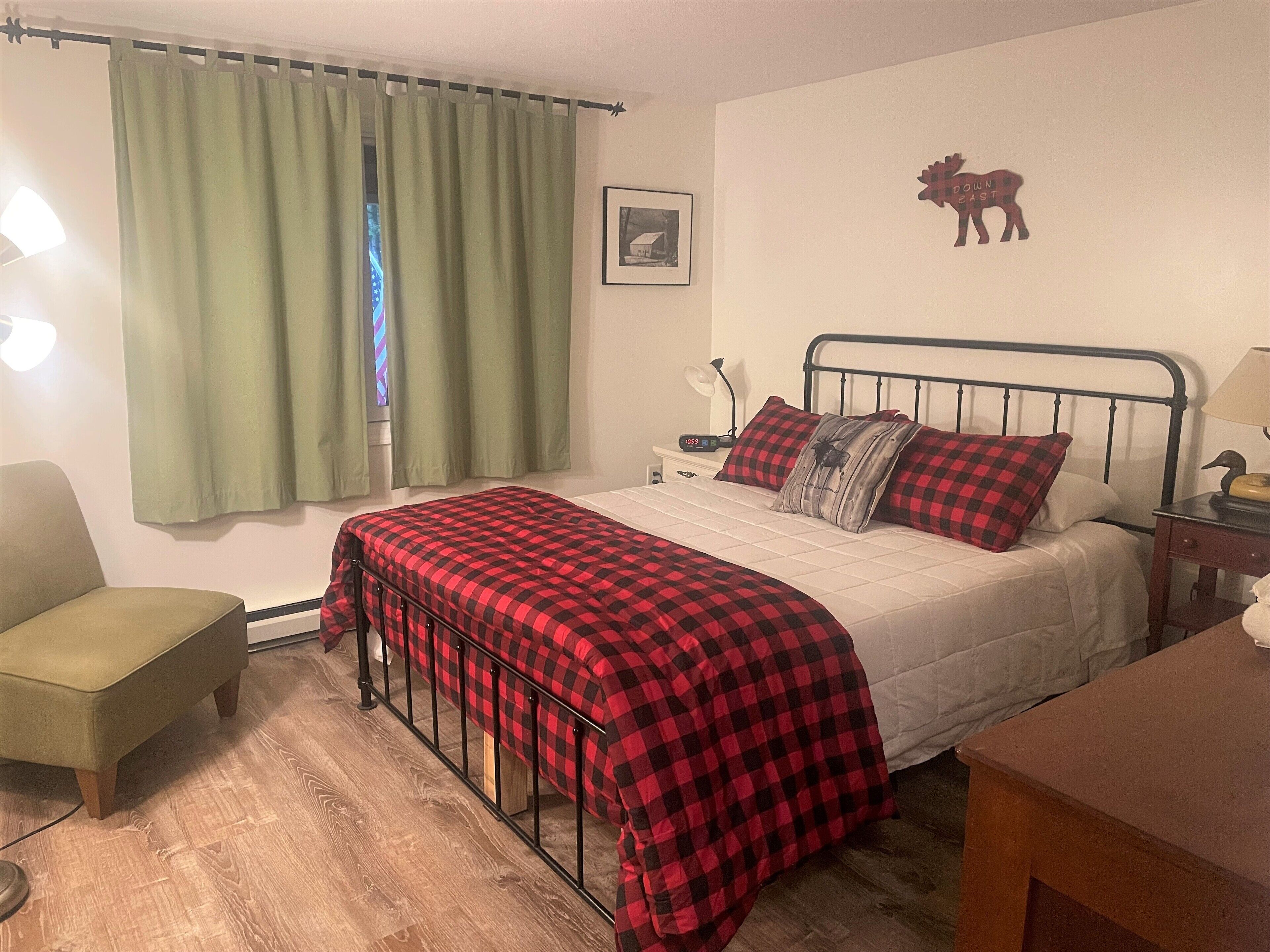 A bedroom with a bed, a chair, a nightstand, and a wall-mounted lamp.