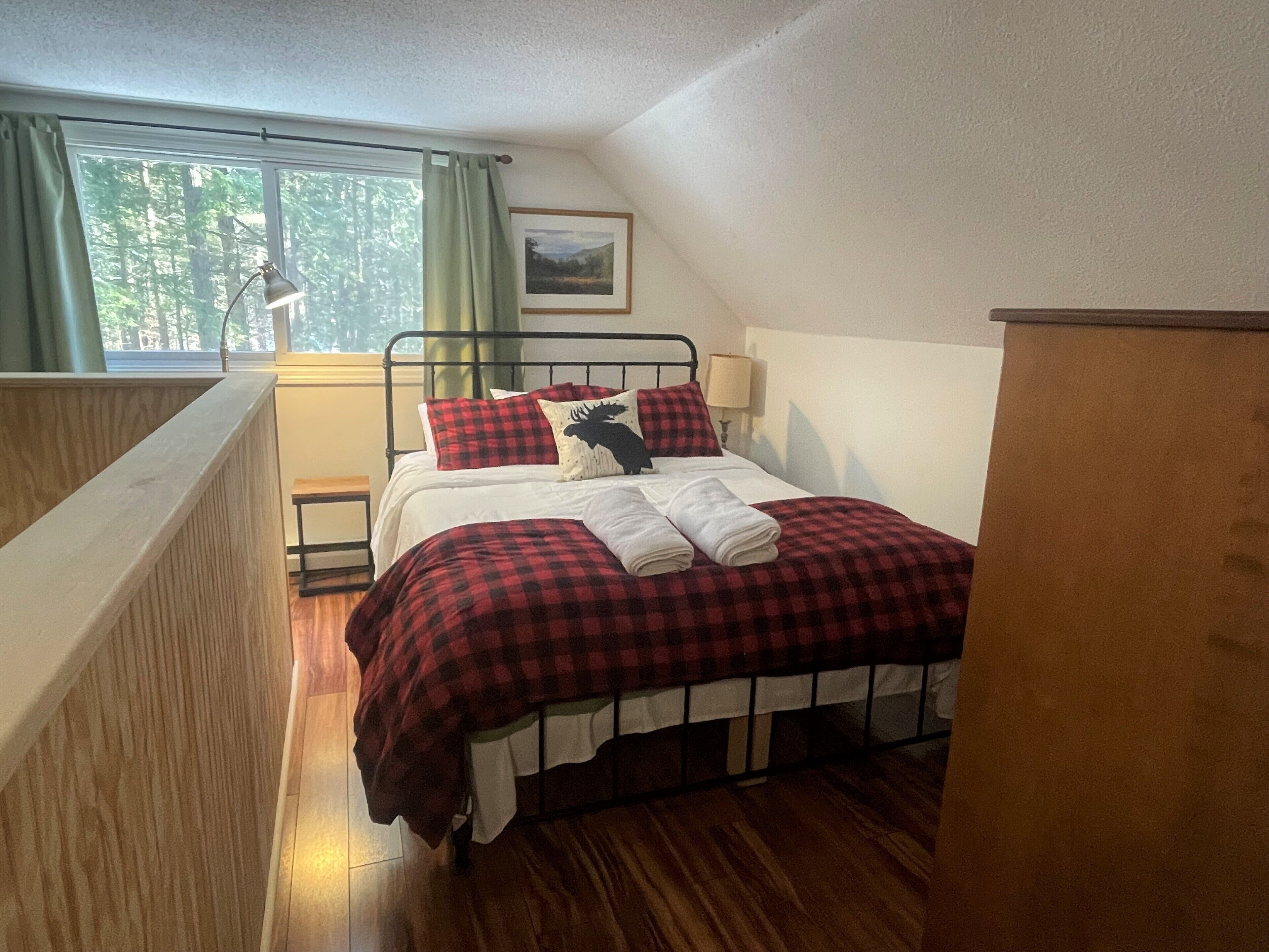 A bedroom with a bed, a window with curtains, a picture on the wall, and a wooden floor.