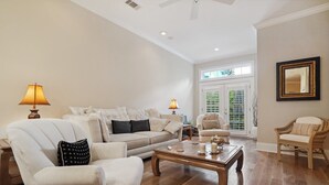 A spacious living room with a high ceiling, a large window, and a view of greenery outside. - 10 Palm Villas Court (St Simons Island)