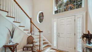 A staircase with white railings and wooden steps, a door with white panels, and a window with a view of trees. - 10 Palm Villas Court (St Simons Island)