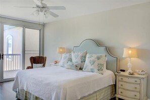A bedroom with a bed, two bedside tables, a ceiling fan, and a window with a view.