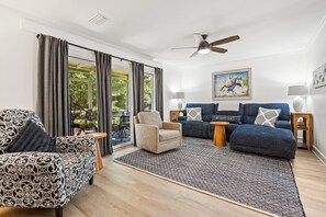 Ein modernes Wohnzimmer mit Sofa, Sesseln und Deckenventilator.