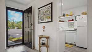 A modern kitchen with white appliances, a small wooden table, and a door leading to a parking area. - Free bikes/pools/tennis/fitness Walk 2 pier/village shops & restaurants! (St Simons Island)