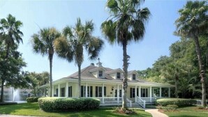 A two-story house with a covered porch, surrounded by palm trees and well-maintained lawns. - Free bikes/pools/tennis/fitness Walk 2 pier/village shops & restaurants! (St Simons Island)