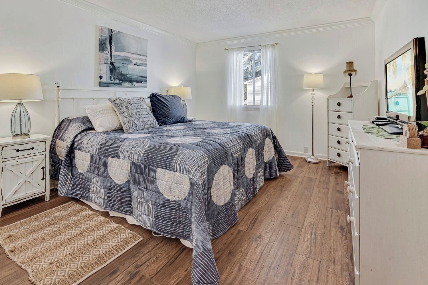A bedroom with a bed, bedside tables, a dresser, a rug, and a window.