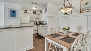 Cozinha com armários brancos, micro-ondas e área de jantar com mesa de madeira e cadeiras brancas.