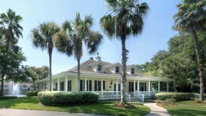 Uma casa de dois andares com varanda, rodeada por palmeiras e um gramado bem cuidado.