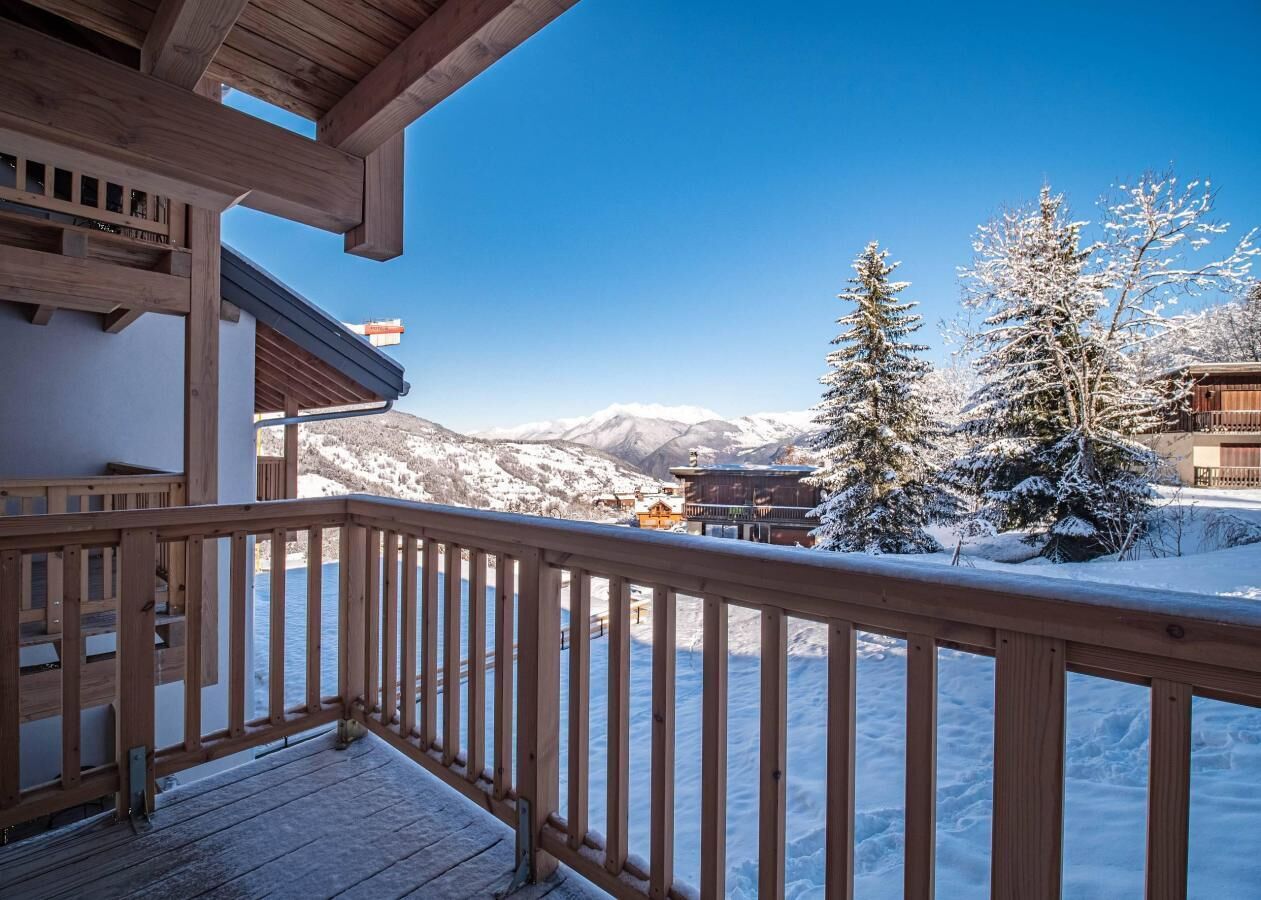 Eine Holzterrasse mit Blick auf schneebedeckte Berge und Bäume.