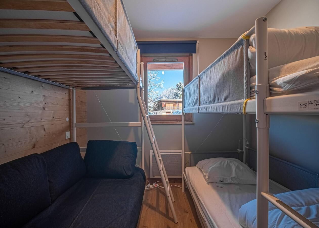 A compact room with bunk beds, a sofa, and a window providing a view of the outside.