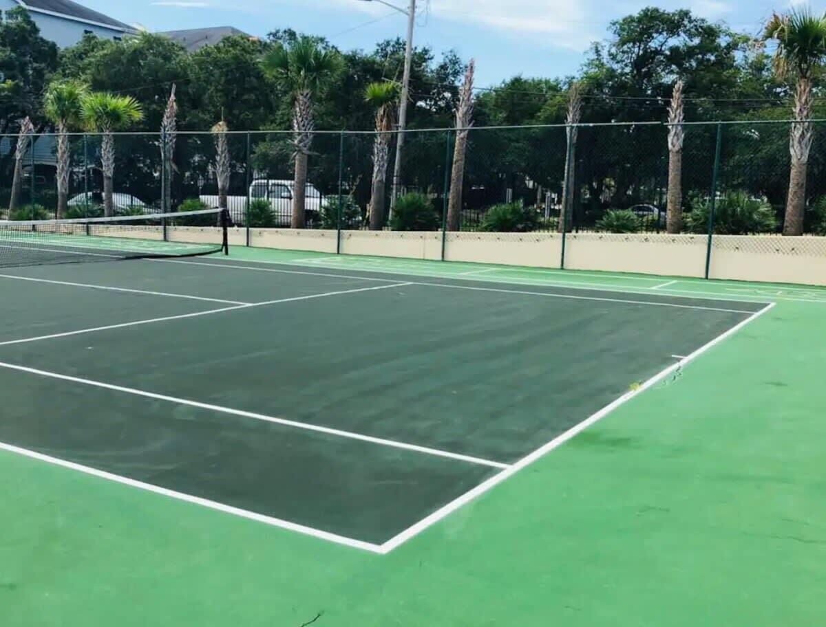 An outdoor tennis court with a green surface and white boundary lines.
