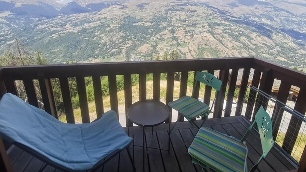 En terrasse med to liggestole og et lille bord, med udsigt over et bjerglandskab.