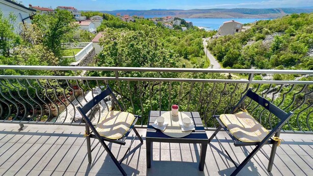 Een balkon met twee stoelen en een tafel, met uitzicht op een schilderachtig meer en de omliggende begroeiing.